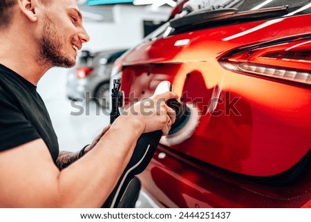 Professional vehicle polishing and detailing service in a modern car workshop. Brightly lit workspace with large led lights. High quality car valeting concept. Royalty-Free Stock Photo #2444251437