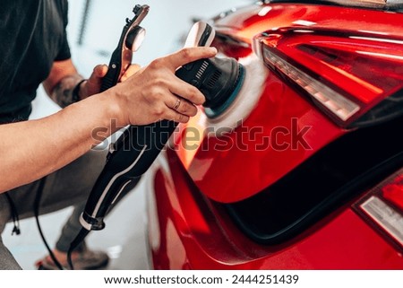 Professional vehicle polishing and detailing service in a modern car workshop. Brightly lit workspace with large led lights. High quality car valeting concept. Royalty-Free Stock Photo #2444251439