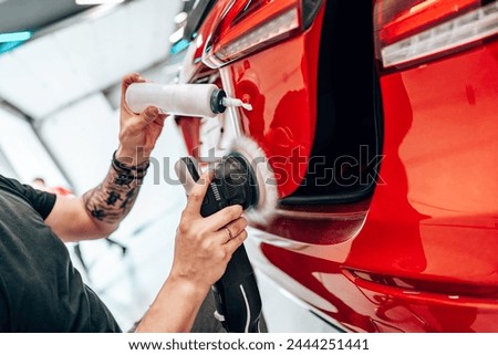 Professional vehicle polishing and detailing service in a modern car workshop. Brightly lit workspace with large led lights. High quality car valeting concept. Royalty-Free Stock Photo #2444251441