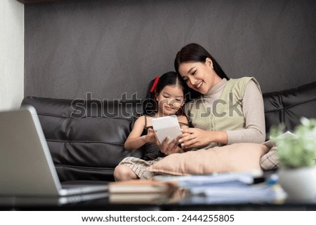 Business woman or mom working with her little daughter at a laptop. Freelance, work from home