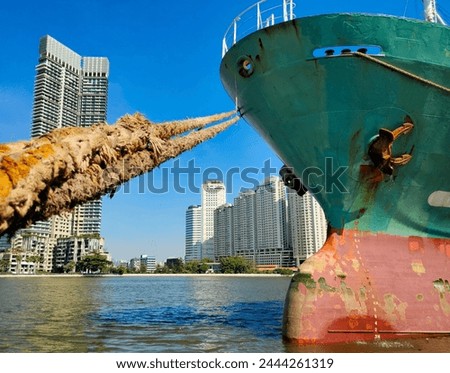 Anchor with large cargo ship's, anchor being pulled. Green and red ship, While docked at the pier by large ropes on the river, in the background is a view of the city's buildings and transport concept
