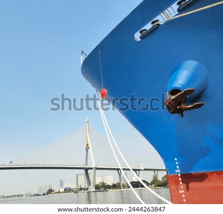 Anchor with large cargo ship's, anchor being pulled. Blue and red ship, While docked at the pier by large ropes on the river, isolate of high brigde with blue sky background and transport concept