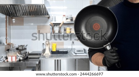 Restaurant kitchen. Frying pan is in cook hand. Cropped cafe employee. Frying pan with non-stick coating. Kitchen utensils. Professional frying pan for cook chef. Culinary equipment. Art focus Royalty-Free Stock Photo #2444266697