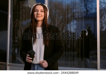 A woman in a suit and headphones dances cheerfully on the street, singing along to music, embodying joy and positivity. A freelancer enjoys the freedom of flexible work hours.