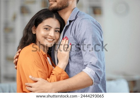 Affectionate hidnu couple hugging while standing in living room interior, free space. Romantic spouses expressing their love