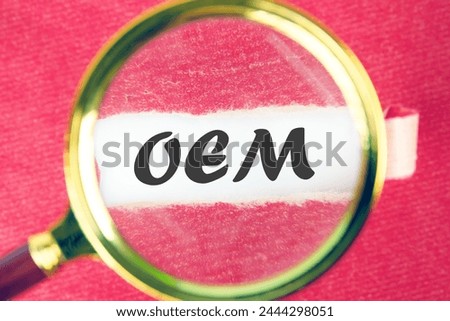 OEM original equipment manufacturer concept. Text through a magnifying glass under a torn piece of paper
