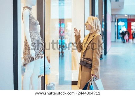 Woman looking through the stores window. Woman with shopping bags in front on store window. Photo of young joyful woman with shopping bags on the background of shop windows