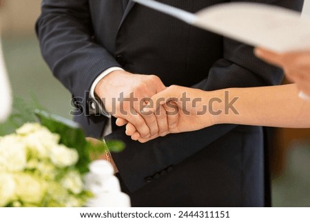 the close-up of a newlywed couple's hands clasped together symbolizes their unity and commitment on their wedding day Royalty-Free Stock Photo #2444311151