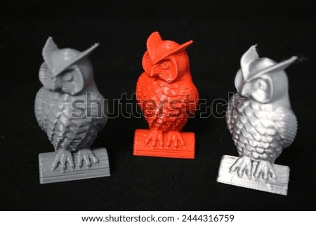 Plastic models of owls, made of plastic, printed on a 3D printer, in gray, silver and red colors. On a black background, close-up, photo.