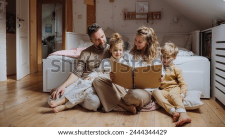 Beautiful family sitting in kids room on floor, looking at old family photos in photoalbum. Calm hygge family moment. Royalty-Free Stock Photo #2444344429