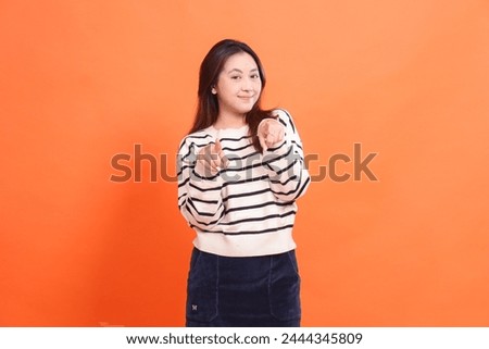 beautiful indonesia girl confident elegant smile standing with both hands pointing to you and looking at the camera isolated on orange background wearing white sweater