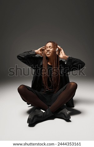 happy african american girl with dreadlocks enjoying the beat in wireless headphones on grey
