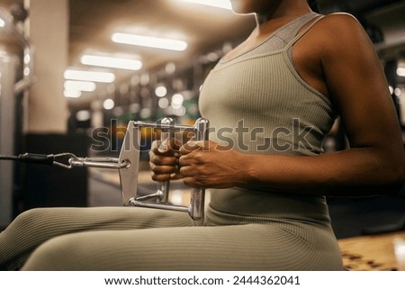 Cropped picture of a powerful fit black sportswoman holding handles on seated cable machine at gym and doing workouts for backs.