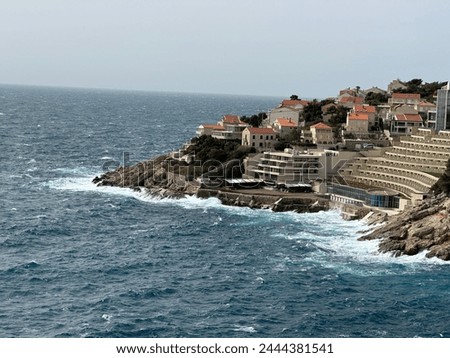 A bright picture of a small area located in Dubrovnik, Croatia with waves crashing against the rocks and some lovely scenery and nature.