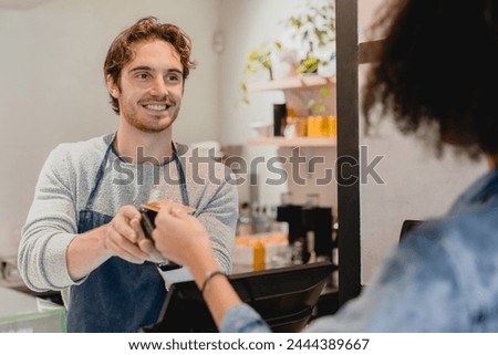 Handsome young caucasian waiter servicing the customer with swiping machine in a cafe. Cashless contactless payment with credit debit card. E-banking e-commerce concept