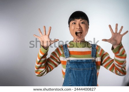 Surprised Asian woman shouting over grey background. Looking at camera. Excited screaming Japanese woman standing isolated over grey background.