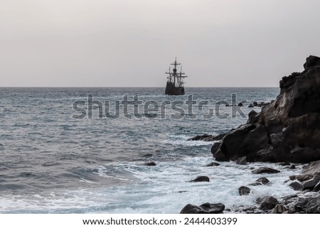 Silhouette of sailing boat ship on the majestic Atlantic Ocean seen from beach Praia Santa Cruz, Madeira island, Portugal, Europe. Sunlight reflection on the calm water surface of the sea. Tranquility