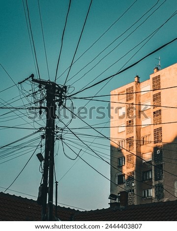 Electricity cables in many directions in front of blue sky and brutalist building