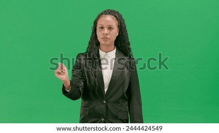 Young female reporter isolated on chroma key green screen background. African american woman tv news host uses virtual screen, swiping gesture.