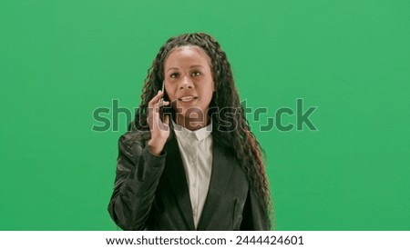 Young female reporter isolated on chroma key green screen background. African american woman tv news host walking and talking on smartphone.