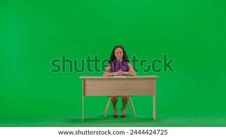 Female in dress sit at the desk isolated on chroma key green screen background. Full shot african american woman tv news host sitting talking looking at camera.