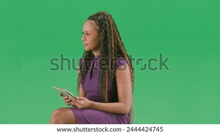 Female in dress isolated on chroma key green screen background. African american woman tv news host sitting holding tablet and taking interview.