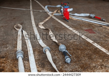 Red fire extinguisher cylinder with unwound fire hoses. Royalty-Free Stock Photo #2444427309