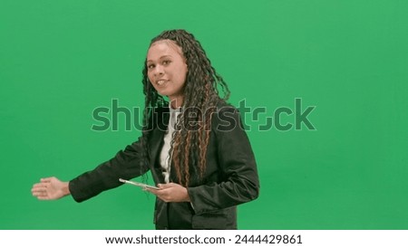 Young female reporter isolated on chroma key green screen background. African american woman tv news host holding tablet, shows empty area.