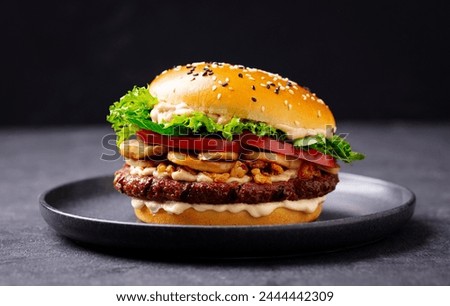 Burger with beef, cheese, vegetables on black plate. Dark Background. Close up.