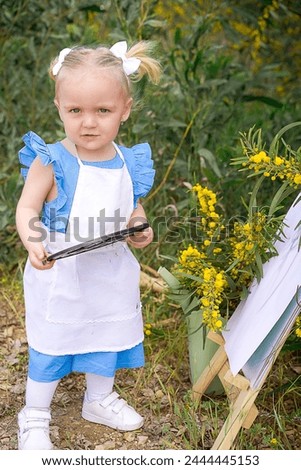 The little girl is drawing! Girl in a blue dress girl draws in nature