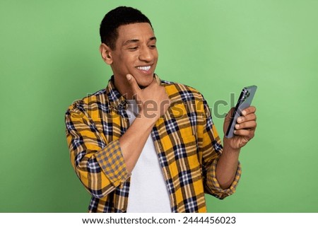 Photo of young positive man touch chin looking at his notepad in smartphone planning schedule day isolated on green color background