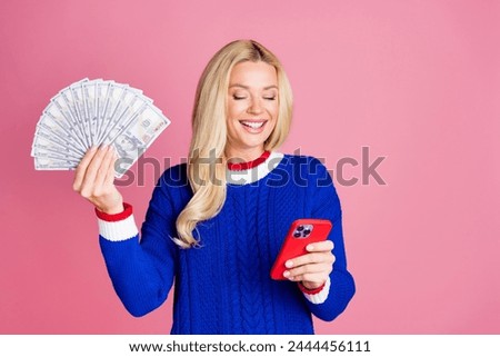 Photo of pretty lady use smart phone hold cash empty space wear blue sweater isolated on pink color background