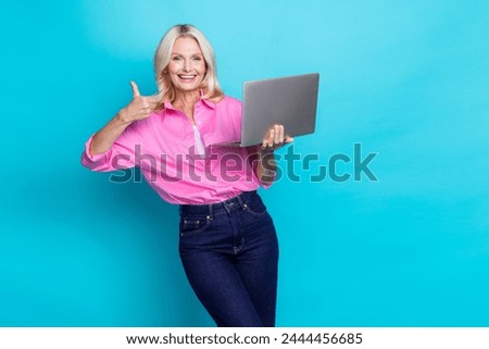 Photo of pretty pensioner female holding laptop thumb up approve wear trendy pink smart casual outfit isolated on cyan color background