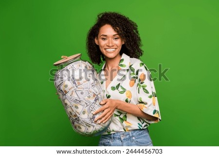 Photo of cheerful shiny lady wear print shirt collect savings glass jar isolated green color background