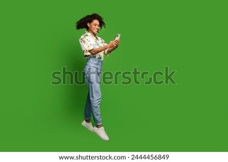 Full length photo of sweet excited lady wear print shirt jumping high texting modern device empty space isolated green color background