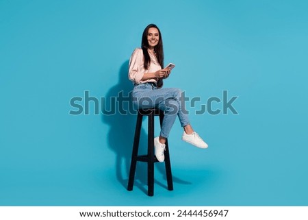 Full length photo of pretty shiny lady dressed beige shirt sitting chair texting modern gadget isolated blue color background
