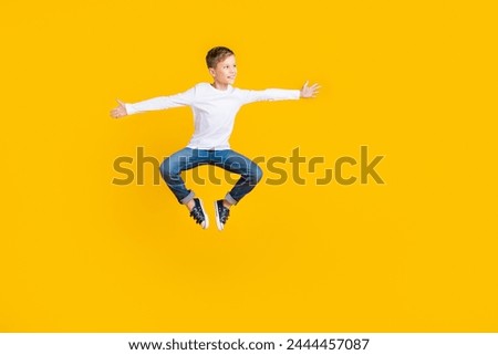 Full length photo of positive impressed kid dressed white shirt jumping high arms sides empty space isolated yellow color background Royalty-Free Stock Photo #2444457087