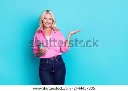 Photo portrait of pretty pensioner female hold device empty space wear trendy pink smart casual outfit isolated on cyan color background