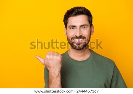 Photo of cool positive guy dressed green t-shirt pointing thumb empty space isolated yellow color background