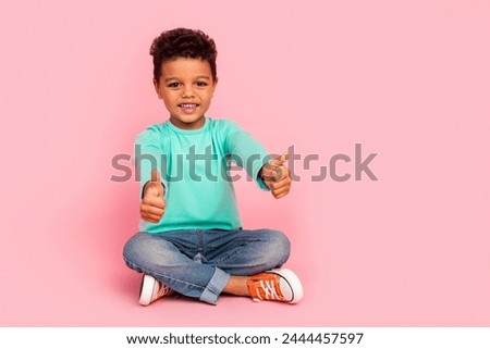 Full length photo of adorable little boy sit floor show double thumb up dressed stylish cyan garment isolated on pink color background