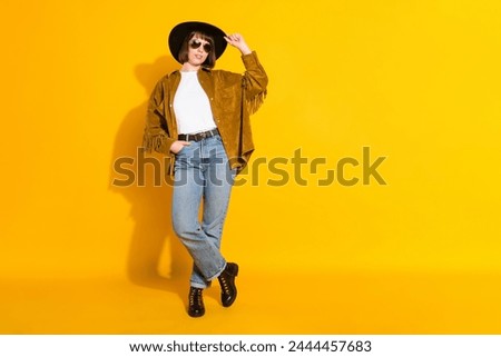 Photo of sweet charming young woman dressed cowboy clothes dark spectacles arm cap empty space isolated yellow color background
