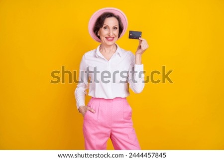 Photo of aged attractive woman happy positive smile hold credit card money salary buyer isolated over yellow color background