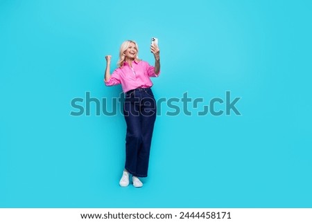 Full size photo of pretty pensioner lady hold device win dressed stylish pink smart casual outfit isolated on aquamarine color background