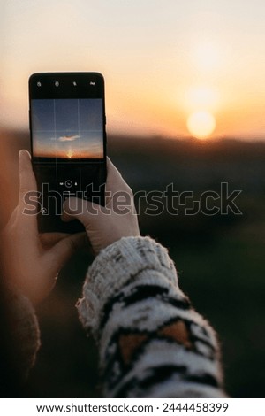 The girl takes a photo of the sky, sunset on the phone. A cloud in the shape of a bird. Vertical photo. A woman is holding a smartphone, phone screen. Warm sunset, dark light, field.
