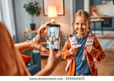 Picture for relatives. Female holding cellular phone for photographing preteen child getting ready for school.The girl stands in the living room with a backpack and poses for a photo for her mother.