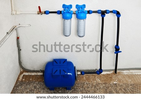 Pressure accumulator or reverse osmosis diaphragm storage tank, and string wound cartridge filters in home water supply system in utility room. Royalty-Free Stock Photo #2444466133