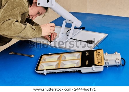 Assembling stand alone solar street light, an electrician attaches solar module and LED luminary to light arm or mounting bracket. Royalty-Free Stock Photo #2444466191