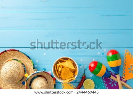 Dive into Cinco de Mayo festivities: top view of sombreros, maracas, lime, chili pepper, flag garland, nachos and confetti on wooden blue background. Great for event promotions