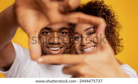 African-american man and woman laughing and showing frame sign with their hands on orange background