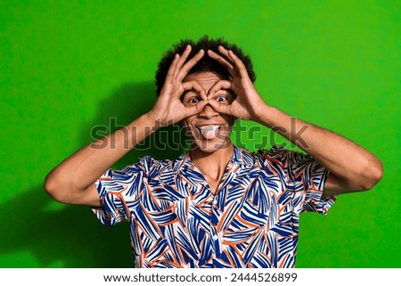 Photo of young funky man stick out tongue joking fooling show okey sign dressed blue print shirt isolated on green color background